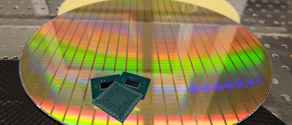 Image of a silicon wafer with chips etched onto it, and a few of the finished chips with their plastic packaging and legs sitting on top